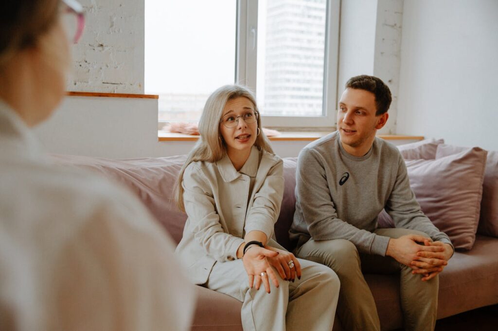 Couple sitting together on a couch during a therapy session, speaking with a therapist in a calm, supportive setting