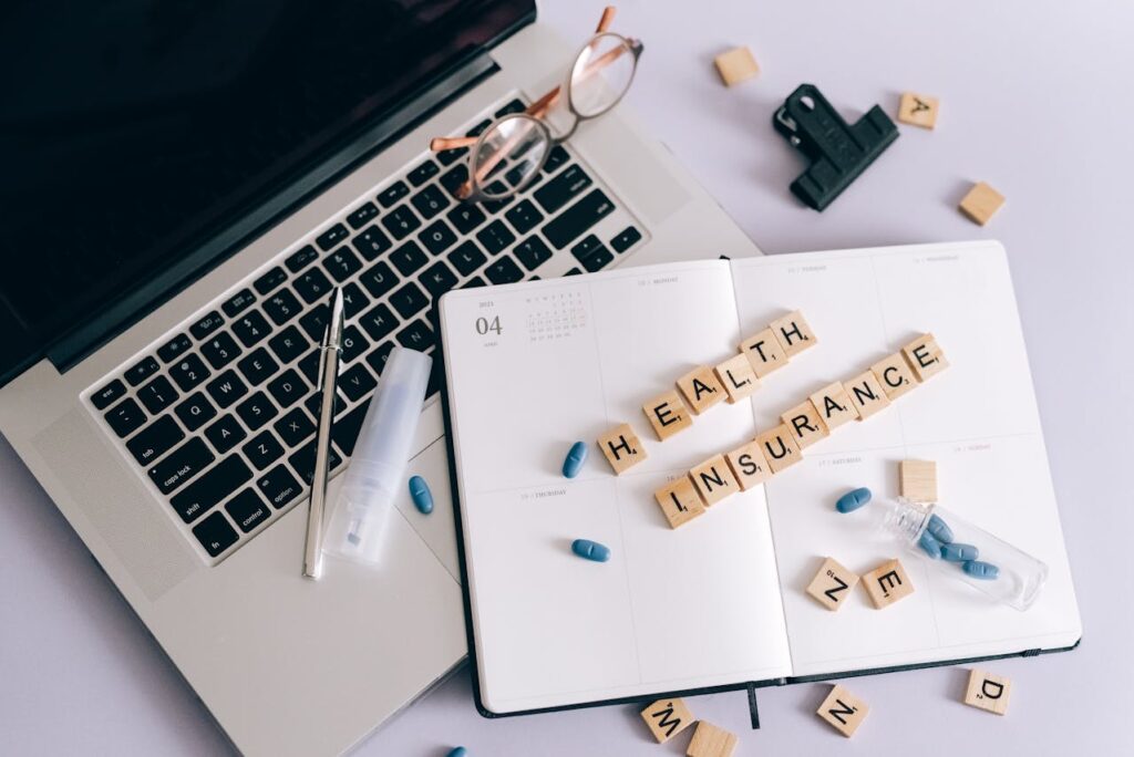 High-angle photo of an open laptop with the words "Health Insurance" written in Scrabble tiles.