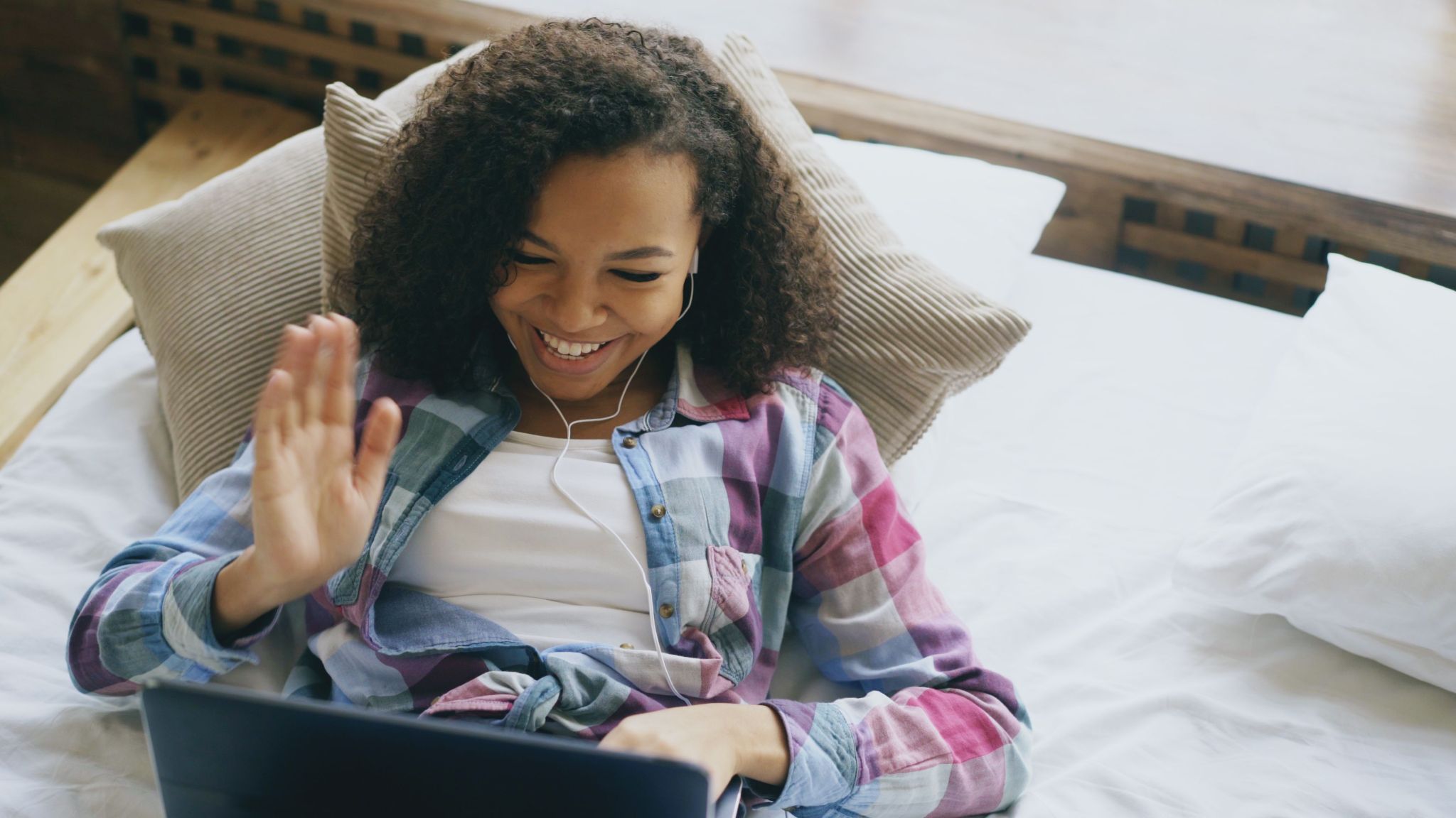 A woman smiles and waves during a video call on her laptop.