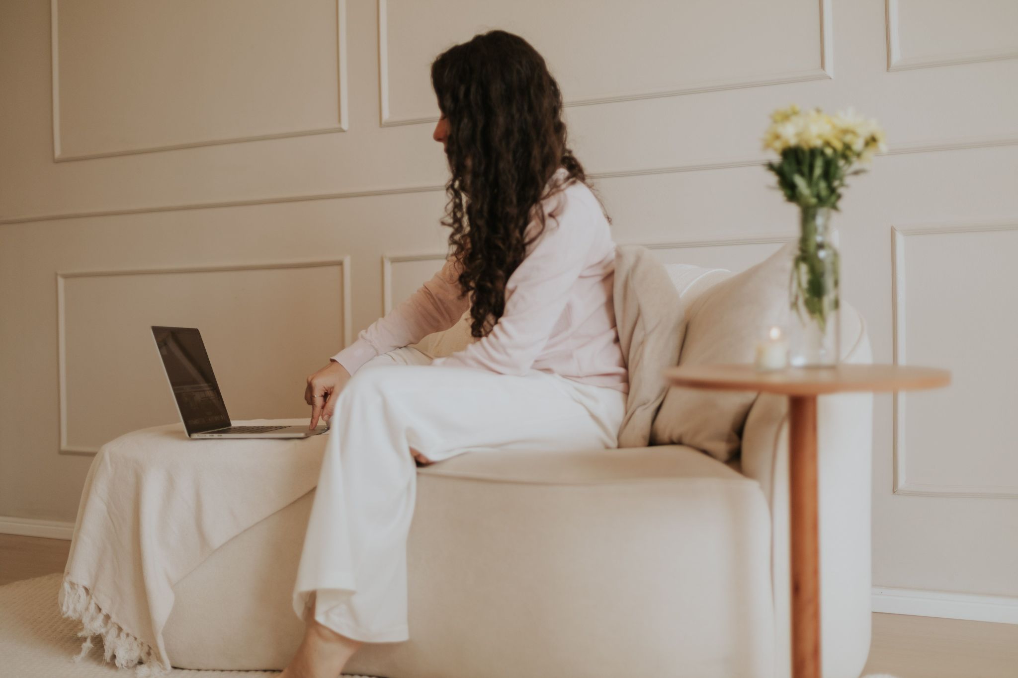 A woman sits in a comfortable chair, looking at her laptop.